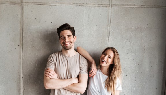 lächelnde junge Frau und junger Mann vor einer Betonwand