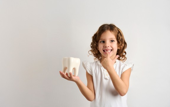 Mädchen hält einen großen Zahn in der Hand und zeigt auf ihre Zahnlücke