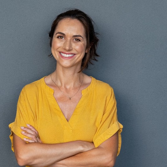 lächelnde Frau mit gelber Bluse lächelt vor dunkelblauer Wand